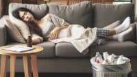 Femme allongée dans un canapé, endormie après une séance d’hypnose, elle est en plein sevrage de ses médicaments pour dormir, qu’elle a jeté dans une poubelle à côté d’elle.